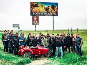 Veterans Charity Ride (VCR) group under South Dakota roadside billboard with red sidecar. Photo by Jonathan Shelgosh.